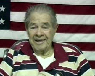 Smiling older man in front of American flag.